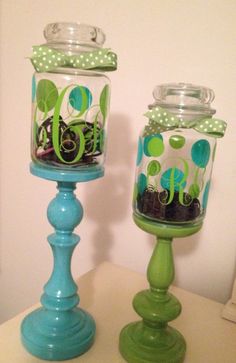 two glass jars with green and blue designs on them sitting on a table next to each other