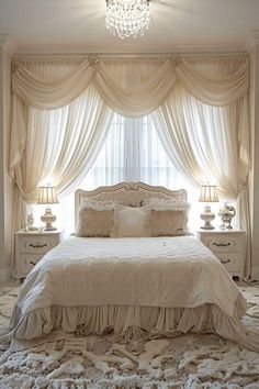 a white bed sitting under a chandelier next to two lamps on either side of a window