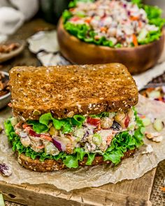 a sandwich with lettuce, tomato, and other vegetables on it next to a bowl of salad