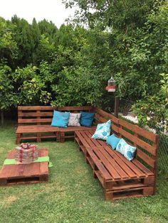 a wooden bench sitting in the middle of a lush green field with blue pillows on it