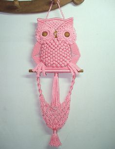 a crocheted pink owl hanging from a hook on a white wall next to a wooden branch