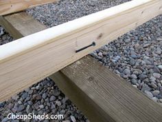 a wooden bench sitting on top of gravel next to a pile of wood planks