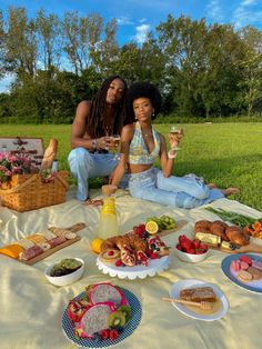 two women sitting on a blanket with food and drinks