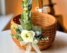 a basket with flowers and greenery on it sitting on a table in front of a mirror