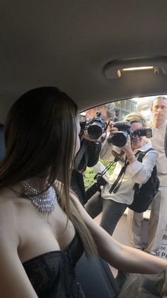 a woman sitting in the back seat of a car with cameras around her and people behind her