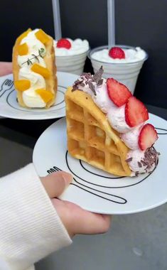 two waffles with strawberries and whipped cream on them are being held by someone