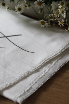 two napkins sitting on top of a wooden table with daisies in the background