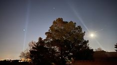 the sun is shining brightly in the night sky over some trees and fenced area