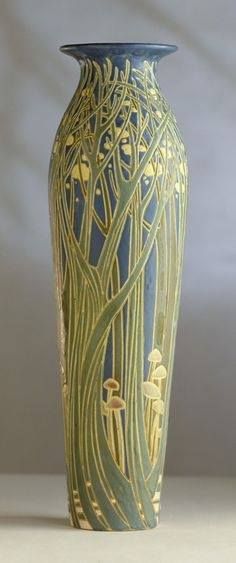 a green vase sitting on top of a white table next to a gray wall in the background