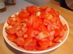 a white bowl filled with chopped tomatoes on top of a wooden table next to a bottle