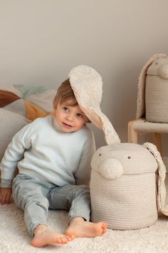 a little boy sitting on the floor next to a stuffed animal and toy bunny hat