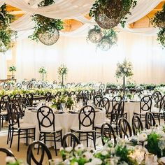 tables and chairs are set up for a wedding reception with greenery hanging from the ceiling