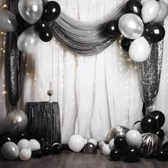 black and white balloons are hanging from the ceiling in front of a backdrop with sheer drapes