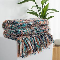 a stack of blankets sitting on top of a table next to a potted plant