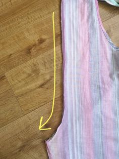 a piece of fabric with yellow thread on it and a pink stripped shirt laying on the floor