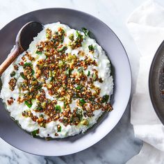 a bowl of mashed potatoes topped with chopped nuts and seasoning next to a spoon