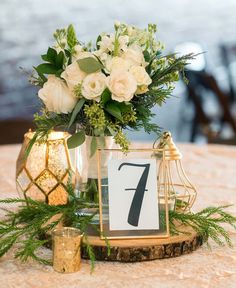 a table topped with a vase filled with white flowers and greenery next to a candle