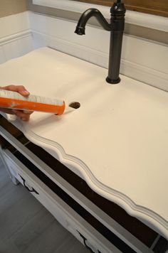 a person using an orange toothbrush to clean a white counter top with black trim