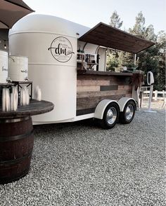 a food truck parked on gravel with an umbrella over the top and two barrels behind it