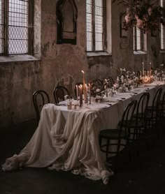 a long table with candles and flowers on it in an old building, surrounded by windows