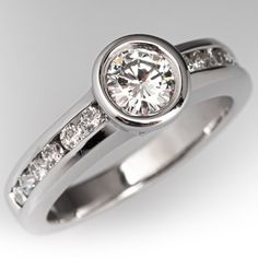 This diamond engagement ring is centered with one (1) round brilliant cut diamond set into a bezel setting. The shoulders of the ring are each accented with six (6) round brilliant cut diamonds set into a channel. The ring measures 7.6mm at the top, rises 6.1mm above the finger, tapering to 3.1mm wide and 1.5mm thick at the base of the shank. It is currently a size 7. Luxury Diamond Ring With Bezel Setting For Women, Luxury White Ring With Bezel Setting, Luxury Birthstone Ring For Women With Bezel Setting, Bezel Set Diamond Engagement Ring, Engagement Rings Channel Set, Bezel Set Engagement Ring, Bezel Engagement Ring, Wedding Ring Necklaces, Bezel Ring