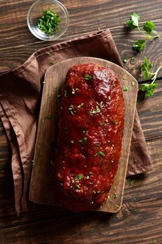 a wooden cutting board topped with meat covered in marinara sauce and garnished with parsley