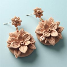 two pairs of flower earrings on a blue surface, one is pink and the other is light brown