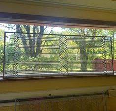 a window that has some kind of design on the glass above it and trees in the background