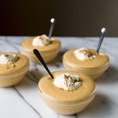 four small bowls filled with food on top of a marble counter topped with spoons