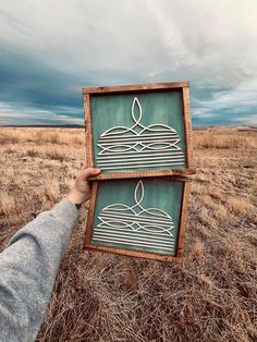 a person holding up a piece of artwork in the middle of a dry grass field