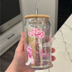 a person holding up a glass jar with pink and white designs on the inside, while wearing a straw hat