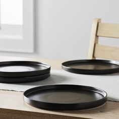 two black plates sitting on top of a wooden table next to a white cloth covered chair