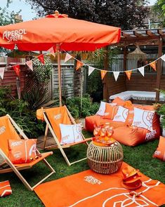 an orange and white patio set up in the grass with chairs, umbrellas and pillows