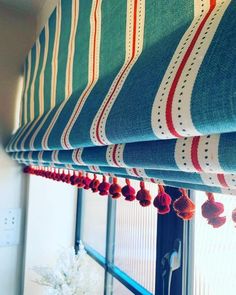 a window with striped curtains and pom - poms hanging from the top of it