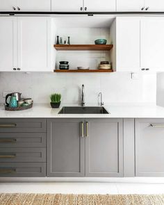 a kitchen with gray cabinets and white counter tops, an open shelf above the sink