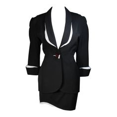 This fabulous Thierry Mugler ensemble is comprised of medium weight wool gabardine with a dramatic sculpted white lapel and cuff detail in white satin. Fitted waist has a single Tri-color abstract square button echoing the white edges of the lapels and cuffs. Medium density shoulder pads. Fitted skirt with a hidden zipper and covered satin snap at back with 3-D white detail at the hem. In overall excellent condition. There is a minute chip at the corner of the white edge of the button. Fully lined in a silk like polyester. Size 42 Please review the measurements provided to ensure a perfect fit. Jacket- Shoulders:17 inches Sleeve:20 inches Bust:38 inches Waist:29 inches Hips:40 inches Skirt- Waist:28 inches Hips: 38 inches Length: 17.25 inches White Skirt Suit, Mugler Black, Suits Outfits, Future Clothes, Skirt Suit Set, Vintage Suits, Black And White Skirt, Thierry Mugler, Satin Jackets