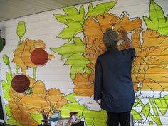 a woman is painting a mural on the side of a building with flowers painted on it