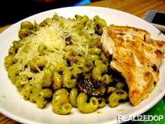 a white plate topped with pasta and meat covered in pesto sauce next to chicken