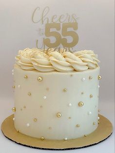 a white cake with gold decorations and a sign that says cheers to 55 on top