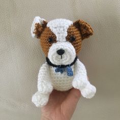 a hand holding a small crocheted dog with a blue bow tie on it's collar