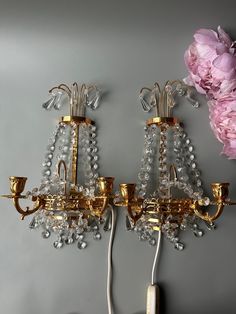 two chandeliers are hanging on the wall with pink flowers in front of them