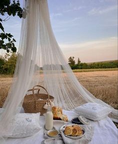 a table with bread and milk on it in the middle of a wheat field under a white canopy