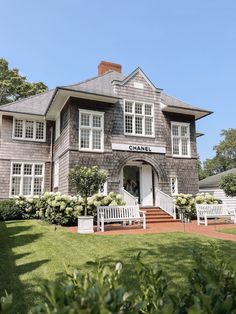 a large gray house with two white benches in front of it and bushes around the entrance