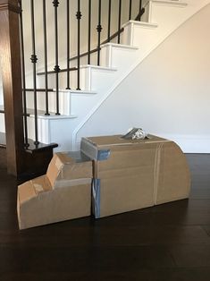 two cardboard boxes sitting on the floor in front of a stair case and banister