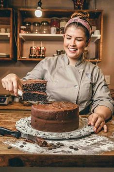 a woman is smiling as she cuts into a chocolate cake on a wooden table with utensils