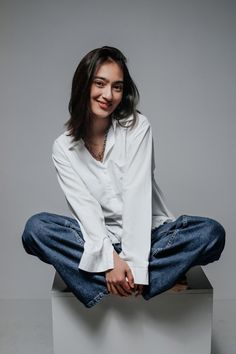 a woman in white shirt and jeans sitting on top of a box with her legs crossed