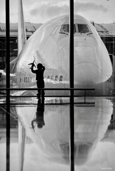 a black and white photo of an airplane at the airport with its reflection on the ground