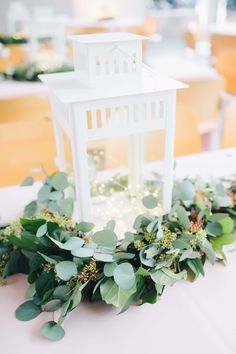 a white lantern is surrounded by greenery on a table