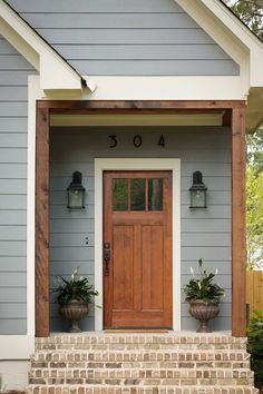 the front door of a house with two planters on the steps and a wooden door