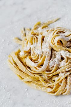 a pile of uncooked pasta covered in powdered sugar on a white surface